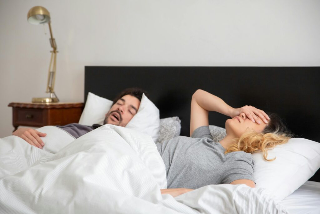 Snoring man sleeps as frustrated woman covers face. Best anti-snoring device can help stop snoring and provide a good nights sleep.