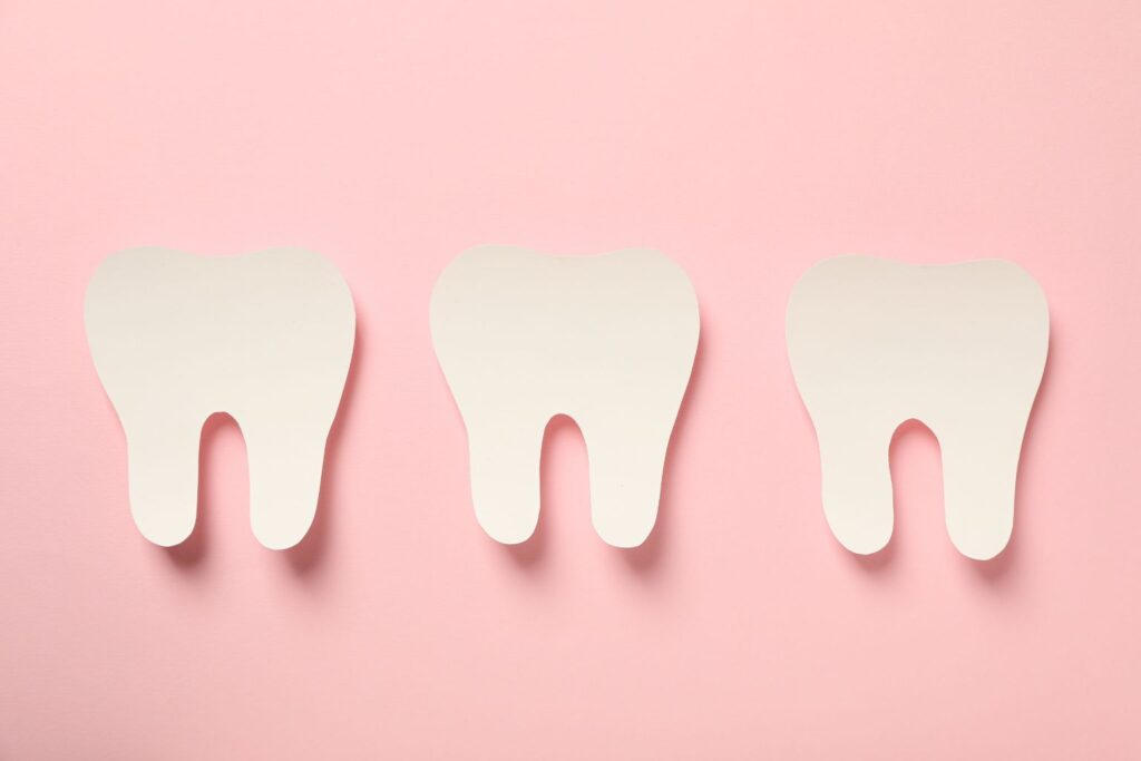 Three paper teeth on pink, teeth whitening concept. Dental health for patients, debunking teeth whitening myths.
